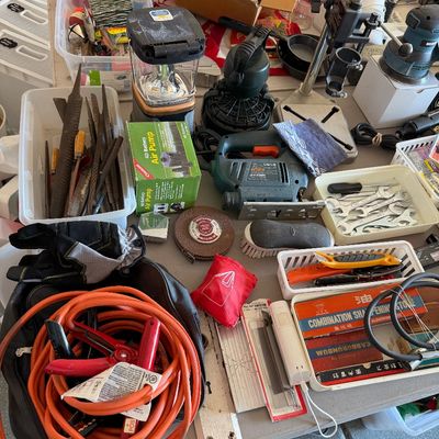 Sale Photo Thumbnail #109: Assorted hand tools, power tools, and garage items including jumper cables, a jigsaw, files, wrenches, and a portable lantern arranged on a table.