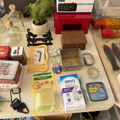 Sale Photo Thumbnail #101: Assortment of household items, including decorative tins, glass decanters, a boxed Insignia alarm clock, a small wooden box, and various crafting and utility supplies.