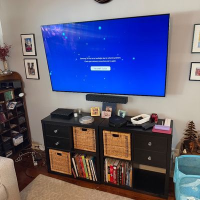 Sale Photo Thumbnail #215: Large wall-mounted Samsung flat-screen television with a matching soundbar, positioned above a pair of black storage units with drawers, woven baskets, and books.