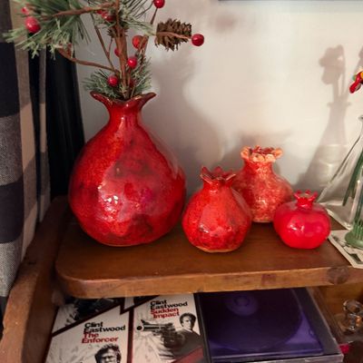 Sale Photo Thumbnail #77: Collection of four red ceramic pomegranate vases in varying sizes, displayed on a wooden shelf alongside DVDs.