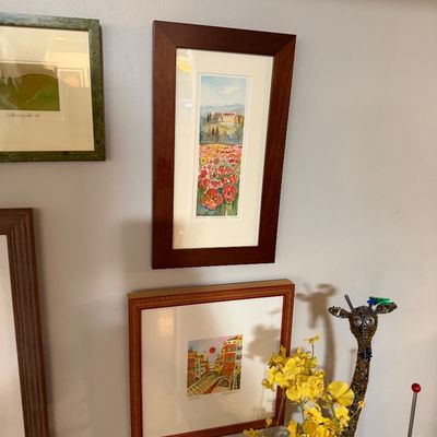 Sale Photo Thumbnail #72: Collection of framed watercolor paintings depicting European landscapes and towns, displayed alongside a beaded giraffe sculpture and yellow faux flowers.