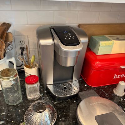 Sale Photo Thumbnail #116: Keurig single-serve coffee maker in brushed silver finish, shown on a kitchen counter alongside a Cuisinart waffle maker and other kitchen accessories.