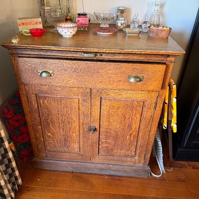 Sale Photo Thumbnail #177: Antique quarter-sawn oak washstand or cabinet featuring a pull-out cutting board, a single wide drawer with brass cup pulls, and a double-door lower compartment.