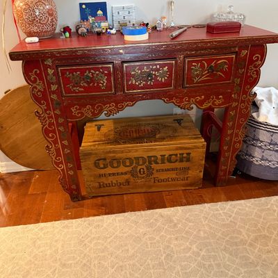 Sale Photo Thumbnail #84: Chinese-style red lacquered console table with hand-painted gold floral details and three drawers, shown with a vintage Goodrich Rubber Footwear wooden crate underneath.