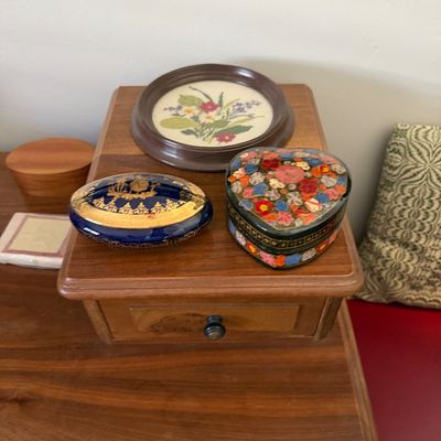 Sale Photo Thumbnail #11: Assorted decorative items including a small wooden single-drawer chest, a framed floral needlepoint, a cobalt blue and gold porcelain trinket box, and a heart-shaped floral lacquer box.