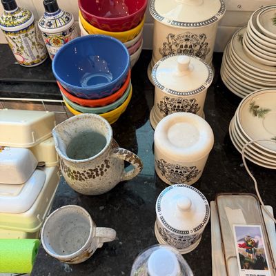 Sale Photo Thumbnail #136: Assorted kitchenware including a set of Fortnum & Mason ceramic canisters, colorful nesting bowls, a rustic stoneware pitcher and mug, and a stack of pinecone-patterned plates.