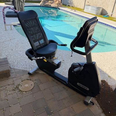 Sale Photo Thumbnail #172: Spirit Fitness recumbent exercise bike with a mesh backrest and digital display console, situated outdoors on a brick patio.