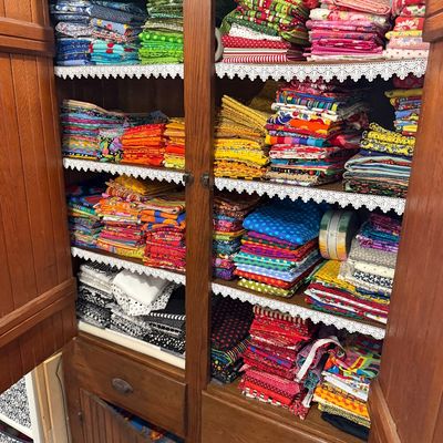 Sale Photo Thumbnail #64: Large collection of colorful quilting fabric fat quarters and yardage, neatly organized by color in a vintage wooden cabinet with lace-trimmed shelves.