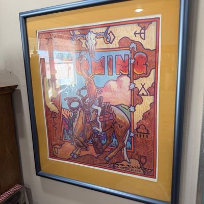 Sale Photo Thumbnail #58: Framed and matted Western art print by Buckeye Blake, dated 1992, featuring a cowboy on a bucking horse with 'Wyoming' text and Native American-inspired motifs.