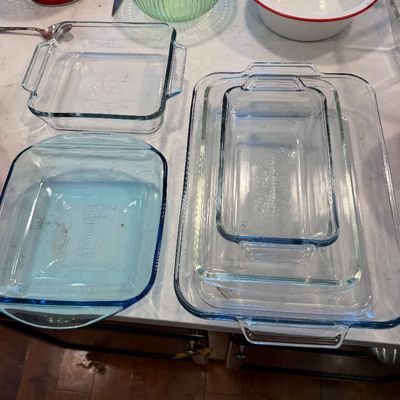 Sale Photo Thumbnail #125: Assorted vintage kitchenware, including clear and blue glass baking dishes, a green ribbed glass bowl, and a white enamel basin with red trim.