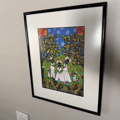 Sale Photo Thumbnail #12: Framed folk art print depicting a family in a vibrant, stylized outdoor setting, presented in a black frame with a white mat.