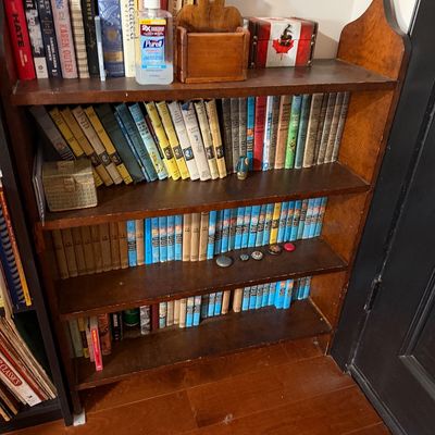 Sale Photo Thumbnail #202: Vintage four-shelf wooden bookcase filled with various books, including vintage Nancy Drew and Hardy Boys series, alongside small decorative items.