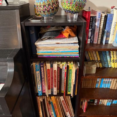 Sale Photo Thumbnail #205: Small black laminate three-shelf bookcase filled with sheet music, songbooks, and baseball caps, topped with two colorful beaded decorative spheres.