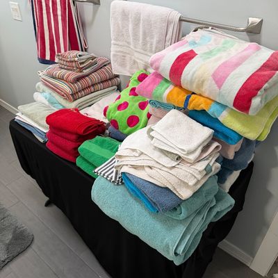 Sale Photo Thumbnail #80: Assorted bath towels, hand towels, and washcloths in various colors and patterns, displayed on a black-clothed table.