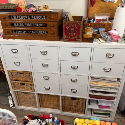 Sale Photo Thumbnail #59: White multi-drawer storage unit with wicker baskets, topped with vintage advertising boxes including an A.W. Faber pencil display case and a Royal Baking Powder crate.