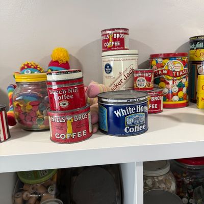 Sale Photo Thumbnail #40: Collection of vintage advertising tins, including Hills Bros. Coffee, Beech-Nut Coffee, White House Coffee, Planters Mixed Nuts, and Cracker Jack, displayed on a white shelf.