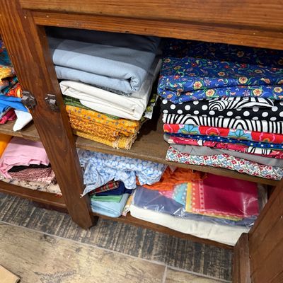 Sale Photo Thumbnail #56: Assorted sewing fabric remnants in various colors and patterns, organized on the shelves of a rustic wooden cabinet.
