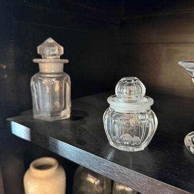 Sale Photo Thumbnail #187: Two vintage clear glass vanity jars with matching glass stoppers, displayed on a dark shelf.