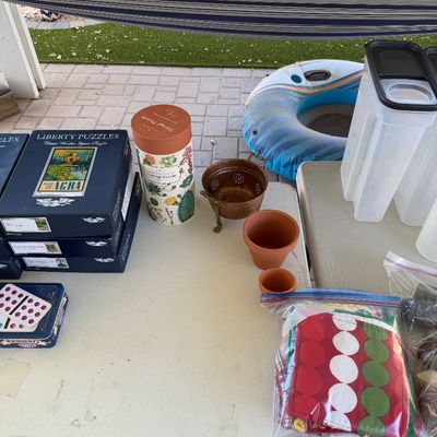 Sale Photo Thumbnail #162: Assorted household items on folding tables, including Liberty Puzzles, a vintage puzzle canister, small terracotta pots, a brass colander, and plastic storage containers.