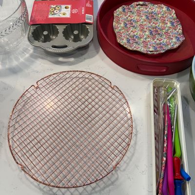 Sale Photo Thumbnail #127: Assorted kitchenware including a copper-toned round cooling rack, a Nordic Ware bundtlette pan, a red serving tray with a floral plate, and various utensils.