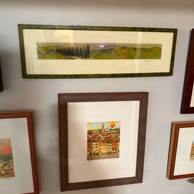 Sale Photo Thumbnail #71: Collection of framed landscape and cityscape art prints, featuring a panoramic Tuscan landscape in a green frame and a colorful Italian village scene in a dark wood frame.