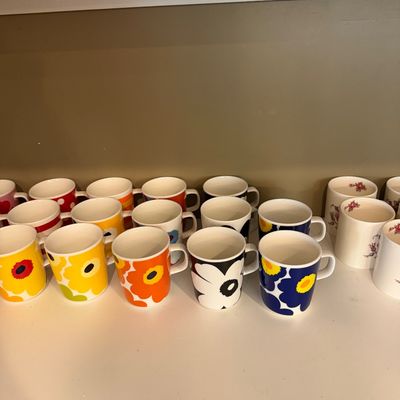 Sale Photo Thumbnail #146: Collection of Marimekko Unikko floral pattern mugs in various colors, displayed alongside other ceramic mugs on a shelf.
