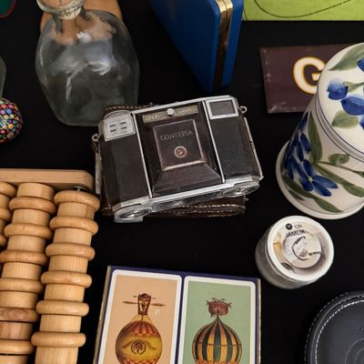 Sale Photo Thumbnail #22: Vintage Zeiss Ikon Contessa folding camera displayed alongside a wooden foot massager, a deck of hot air balloon playing cards, and various small collectibles.