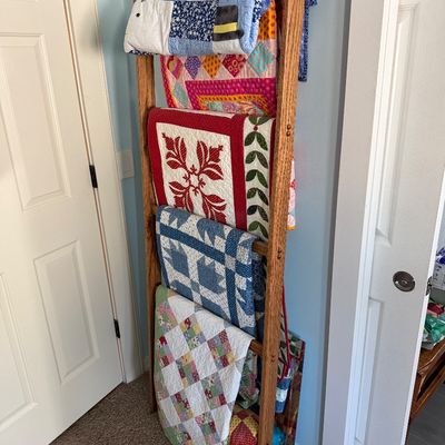 Sale Photo Thumbnail #89: Rustic wooden blanket ladder displaying five colorful, handmade quilts with various patterns including a snowman motif and traditional patchwork designs.
