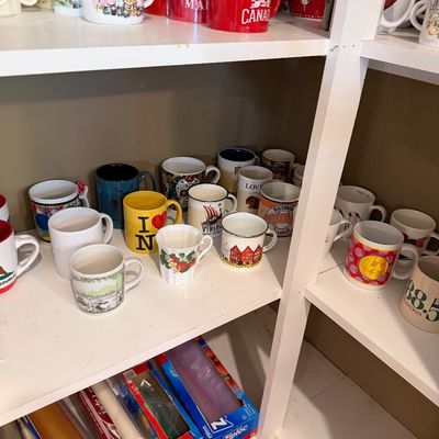 Sale Photo Thumbnail #142: Large collection of vintage and modern novelty coffee mugs displayed on white wooden shelving.