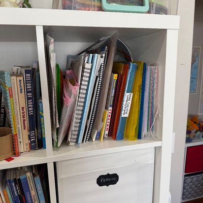 Sale Photo Thumbnail #37: White cube shelving unit filled with craft books, notebooks, folders, and a fabric storage bin labeled "Patterns."