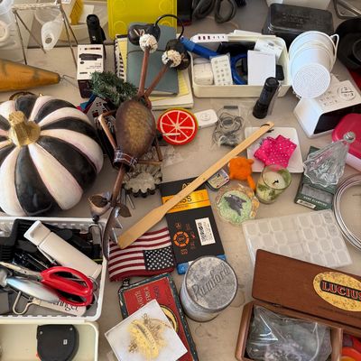 Sale Photo Thumbnail #93: Assorted table of estate sale items, including a black and white painted pumpkin, a vintage Rumford tin, a Lucius wooden box, and various household tools and decor.