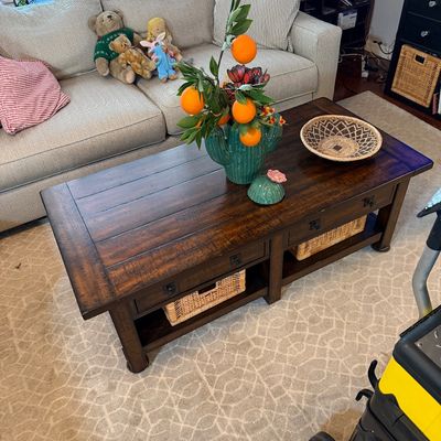 Sale Photo Thumbnail #217: Rustic dark wood coffee table featuring a planked top, two drawers, and a lower shelf with woven storage baskets.