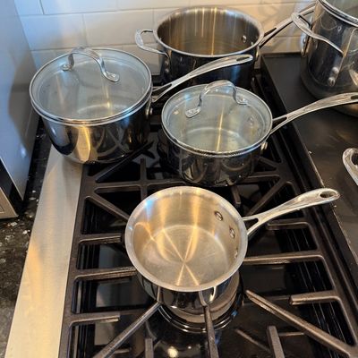 Sale Photo Thumbnail #126: Set of stainless steel pots and saucepans with glass lids, shown in clean, used condition on a gas stovetop.