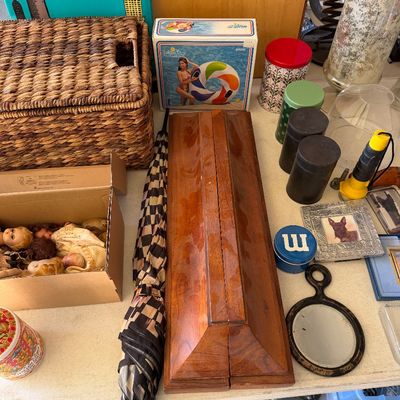 Sale Photo Thumbnail #103: Assorted vintage household items, including a woven wicker basket, a boxed inflatable pool float, a wooden box, a patterned umbrella, and various decorative tins and frames.