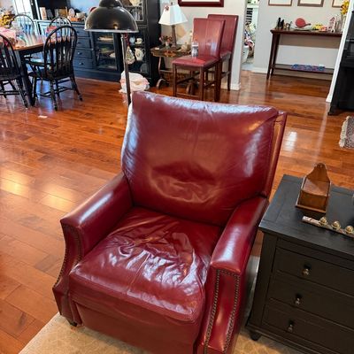Sale Photo Thumbnail #213: Oxblood red leather recliner with brass nailhead trim, showing some wear on the seat cushion.