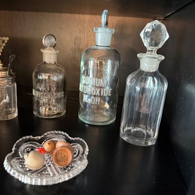Sale Photo Thumbnail #186: Vintage glass apothecary bottles with ground glass stoppers, including labeled bottles for Acid Hydrochloric and Sodium Hydroxide, displayed alongside a small pressed glass dish.
