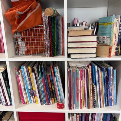 Sale Photo Thumbnail #34: A white cube shelving unit filled with a variety of books, crafting magazines, fabric remnants, and a red storage bin.