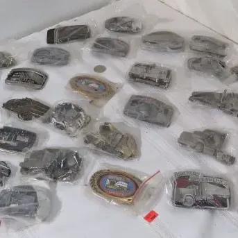 Collection of vintage novelty belt buckles, many individually wrapped in plastic, featuring various designs including trucks, trains, and...