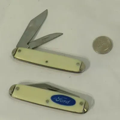 Pair of vintage pocket knives with cream-colored handles, one featuring a blue Ford logo, shown next to a quarter for scale.