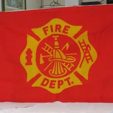 Vintage red and yellow Fire Department flag featuring a Maltese cross emblem with firefighting tools.