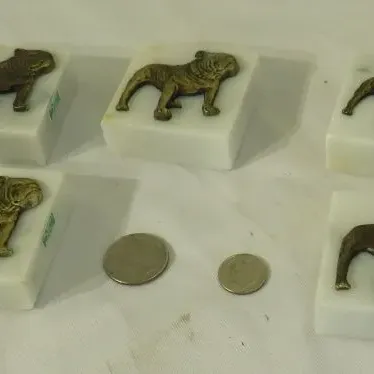 Set of five vintage marble paperweights featuring brass bulldog emblems, shown with coins for scale.