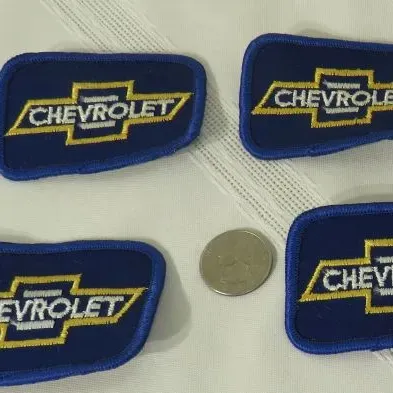 Four vintage embroidered Chevrolet bowtie patches in blue, yellow, and white, shown with a quarter for scale.