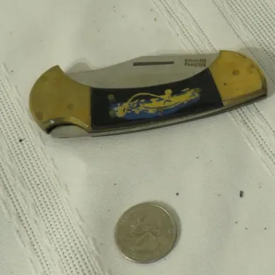 Vintage folding pocket knife with brass bolsters, a black handle inlay featuring a fisherman graphic, and a blade stamped 'Stainless...
