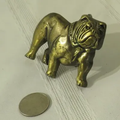Vintage brass Mack Trucks bulldog figurine with a collar, showing some surface wear and patina, pictured next to a coin for scale.
