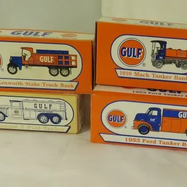 Four vintage Gulf Oil promotional toy truck banks in their original boxes, including a 1925 Kenworth Stake Truck, a 1910 Mack Tanker, a...