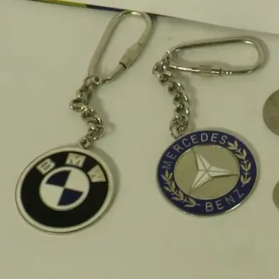 Vintage BMW and Mercedes-Benz enamel keychains with screw-lock clasps, shown next to coins for scale.