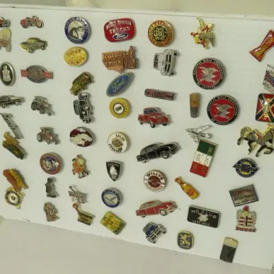 Collection of vintage enamel and metal lapel pins, featuring automotive brands like Ford, GMC, and Plymouth, displayed on a white board.
