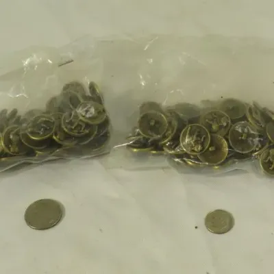 Two plastic bags containing vintage brass-tone metal buttons featuring a raised animal design, shown with coins for scale.