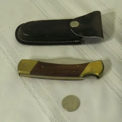 Vintage folding pocket knife with wood and brass handle, shown with its black leather belt sheath and a quarter for scale.