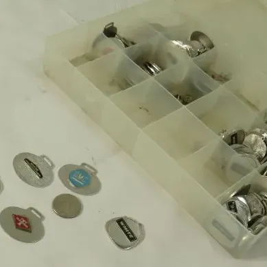 Collection of vintage metal keychains and tags, including GMC and White truck brands, organized in a plastic compartment storage box.